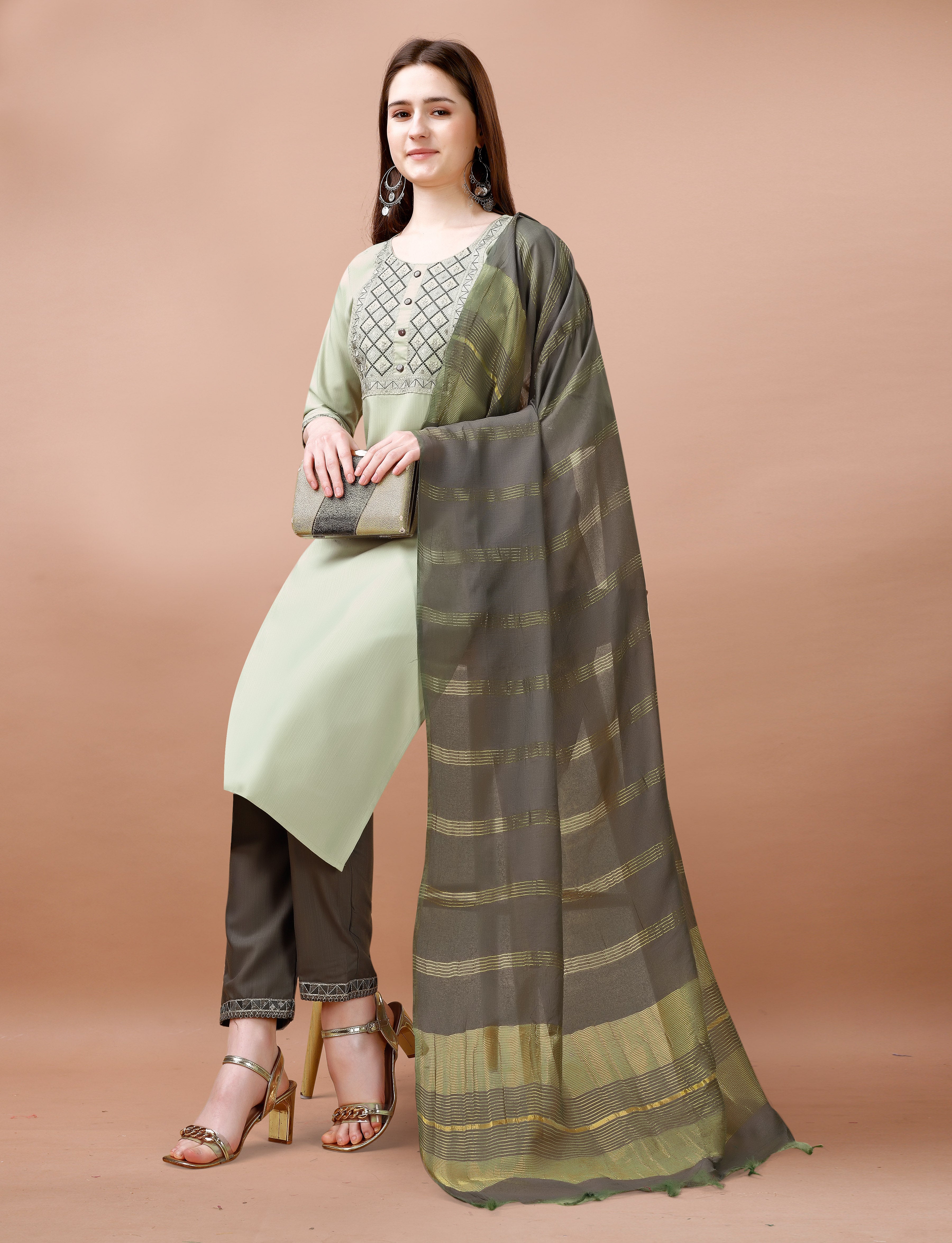 Woman posing gracefully in a sage green embroidered kurta set, showing the full outfit with charcoal grey dupatta and accessories.