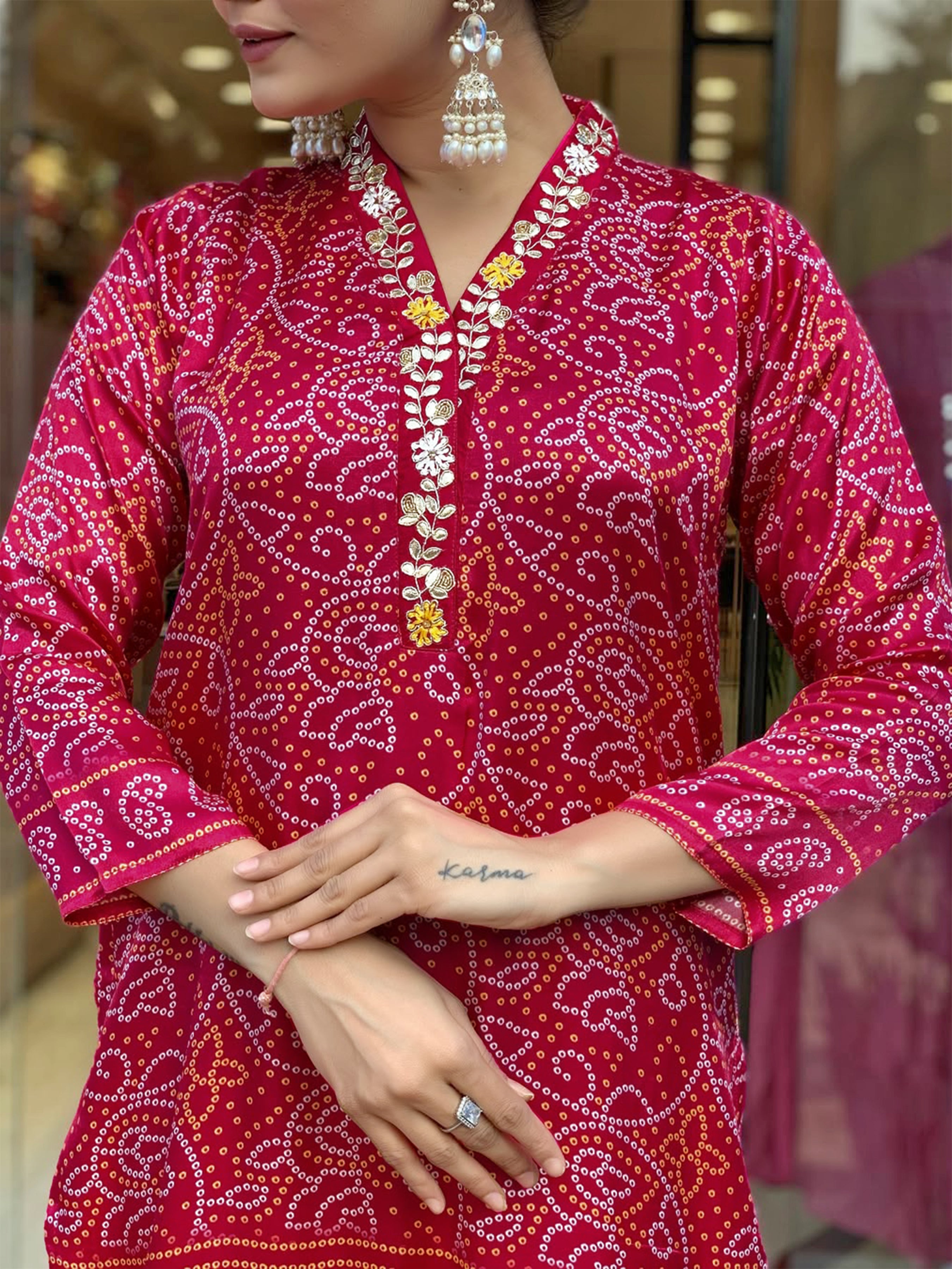 Close-up of a woman wearing a magenta Viscose Silk Kurti with intricate white and gold bandhani-style hand prints and delicate floral embroidery on the V-neckline.