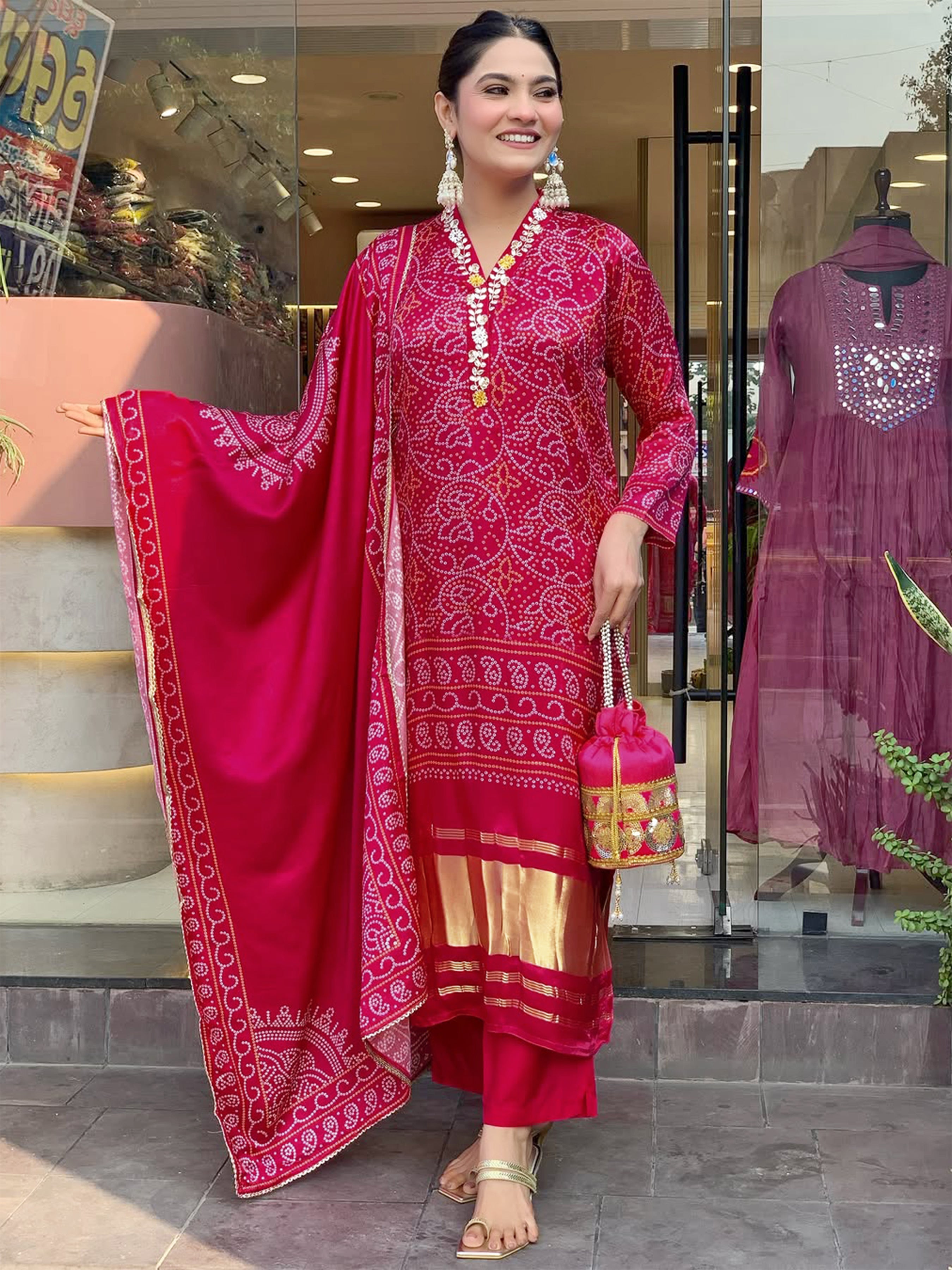 Full-length shot of a smiling woman posing confidently in the magenta NAVYA Kurti set, holding a matching potli bag, emphasizing the complete ethnic ensemble.