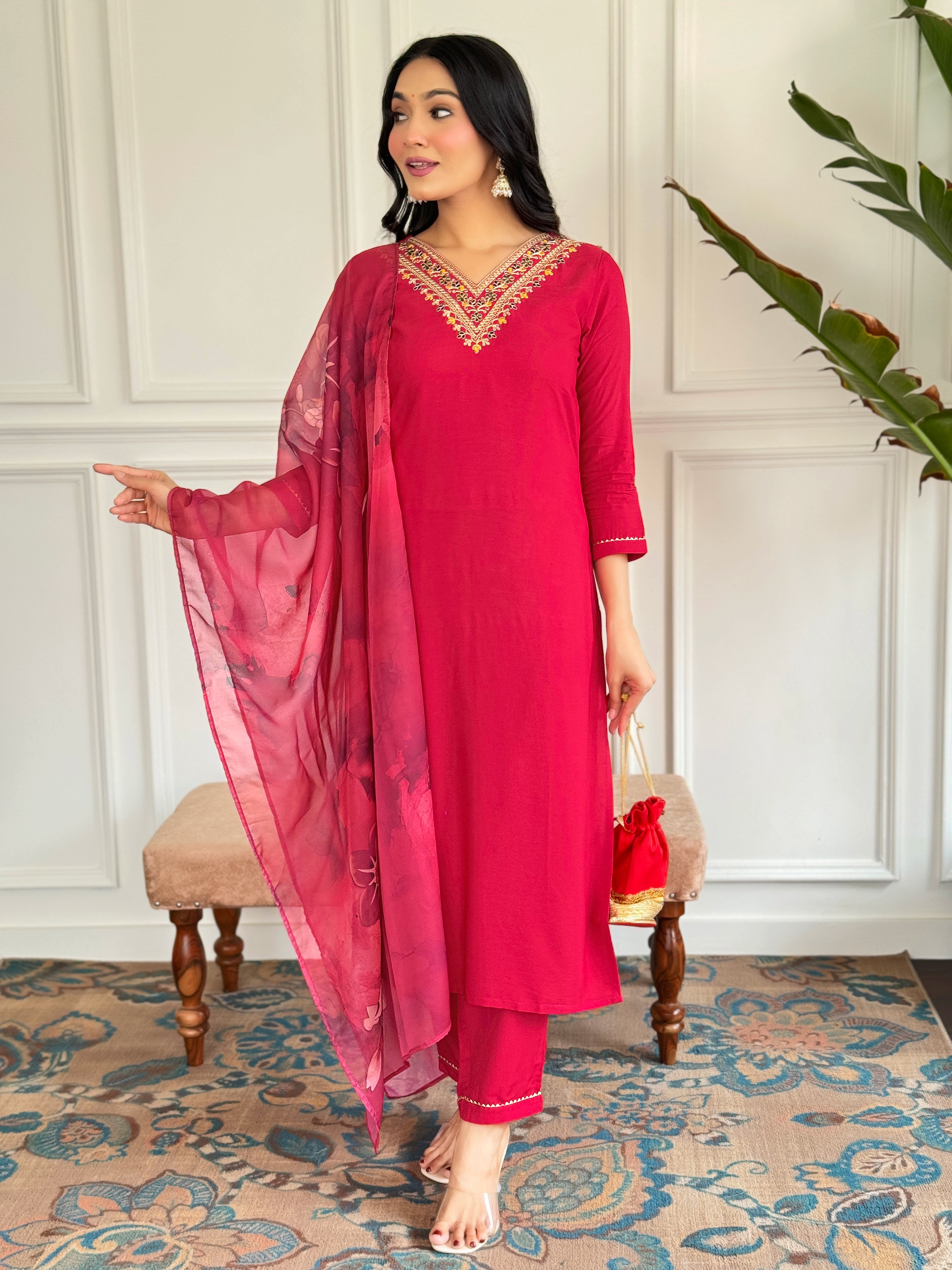 Full-length view of a model showcasing the TRENDBUY red rayon embroidered kurta set with a flowing silk printed dupatta, standing gracefully in a stylish room.