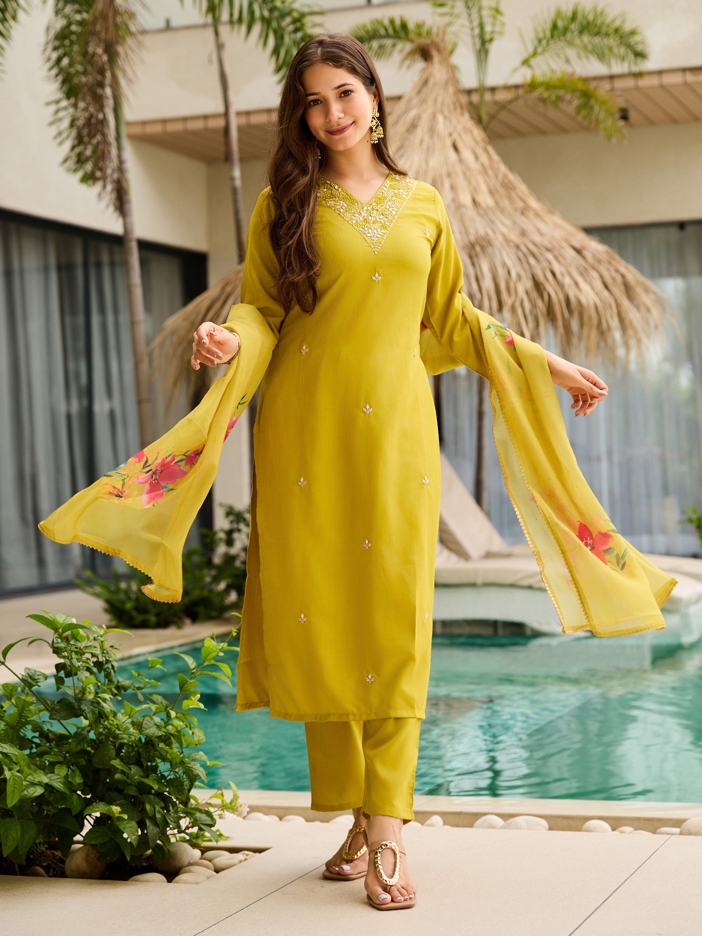 Full shot of model in yellow kurti set, gracefully holding out the floral organza dupatta, by the poolside.
