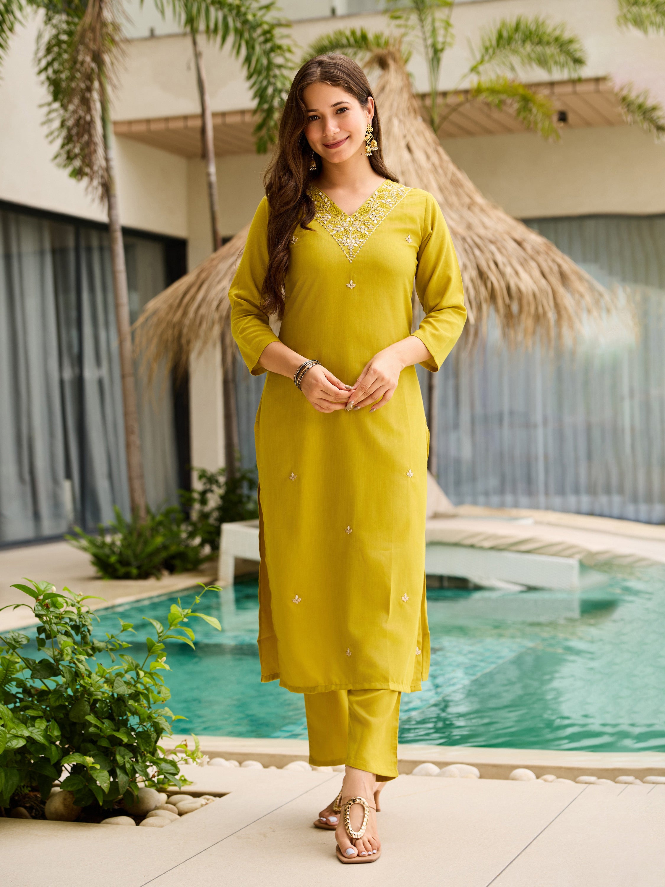 Full length shot of woman in the lemon kurti set, standing front-facing by a tranquil pool setting.
