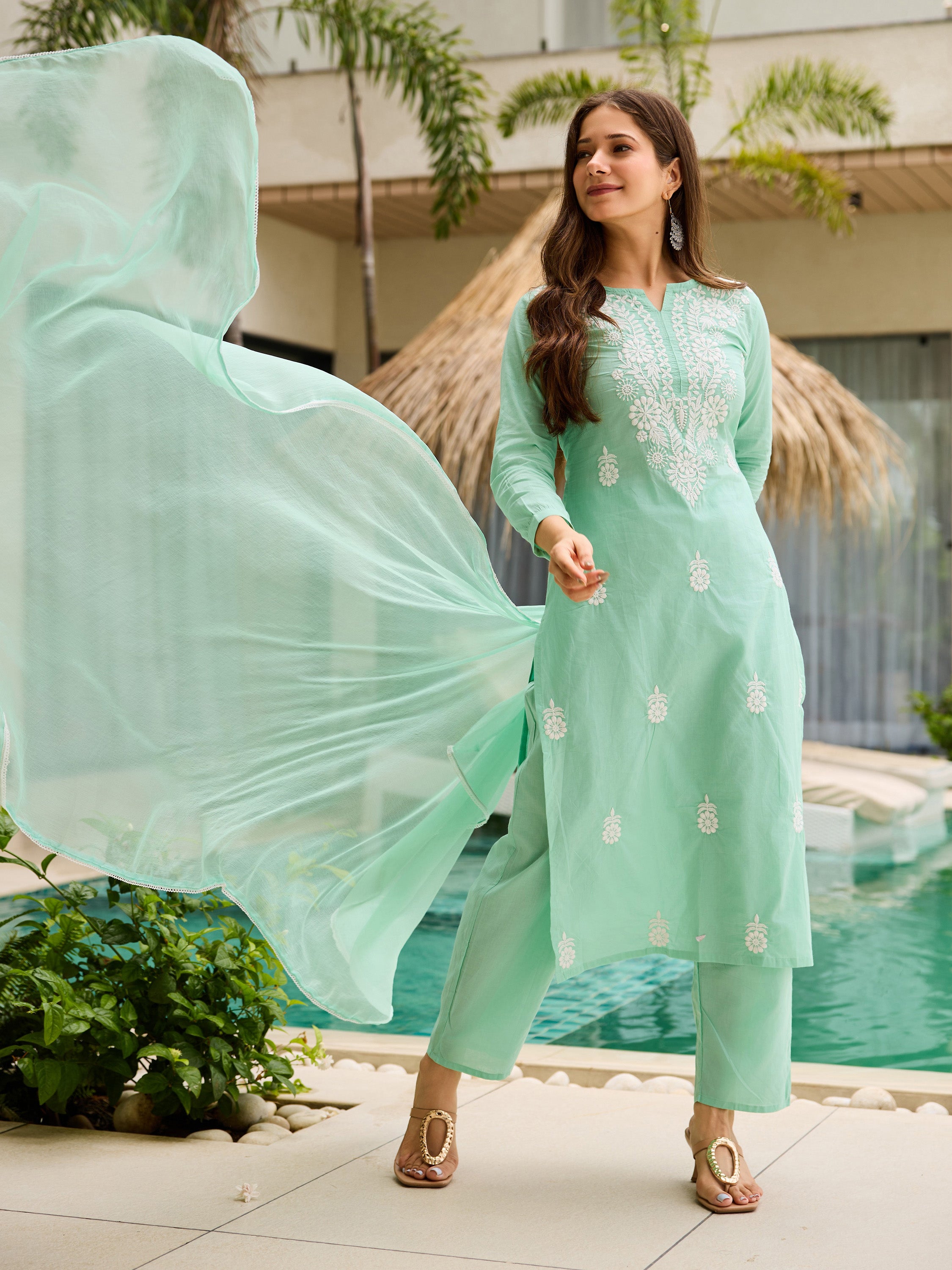 Woman in turquoise kurta set gracefully posing, dupatta flowing in air with tropical background