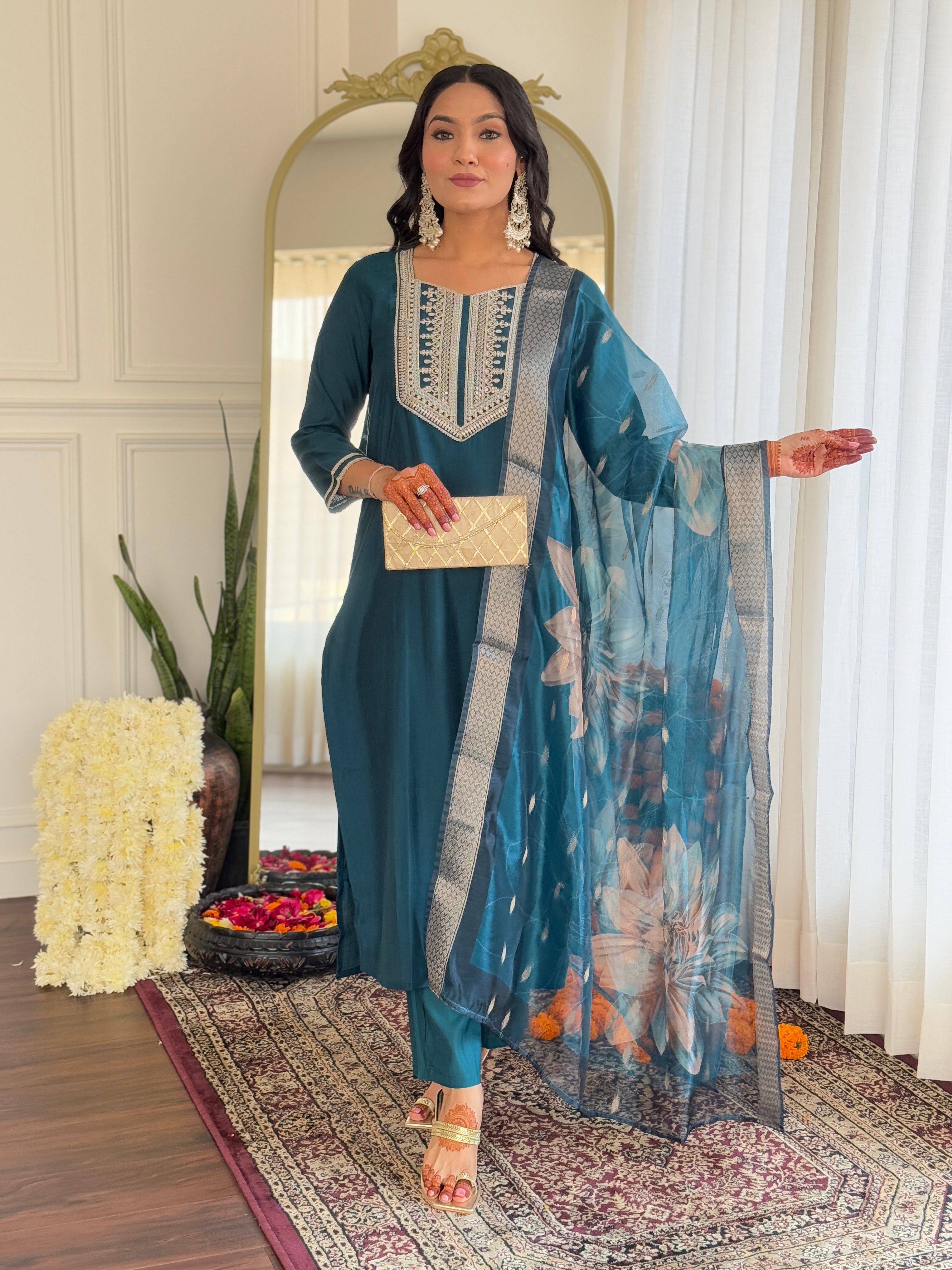 Elegant woman posing in a full teal embroidered BSY viscose kurti pant set with floral organza dupatta, holding a golden clutch.