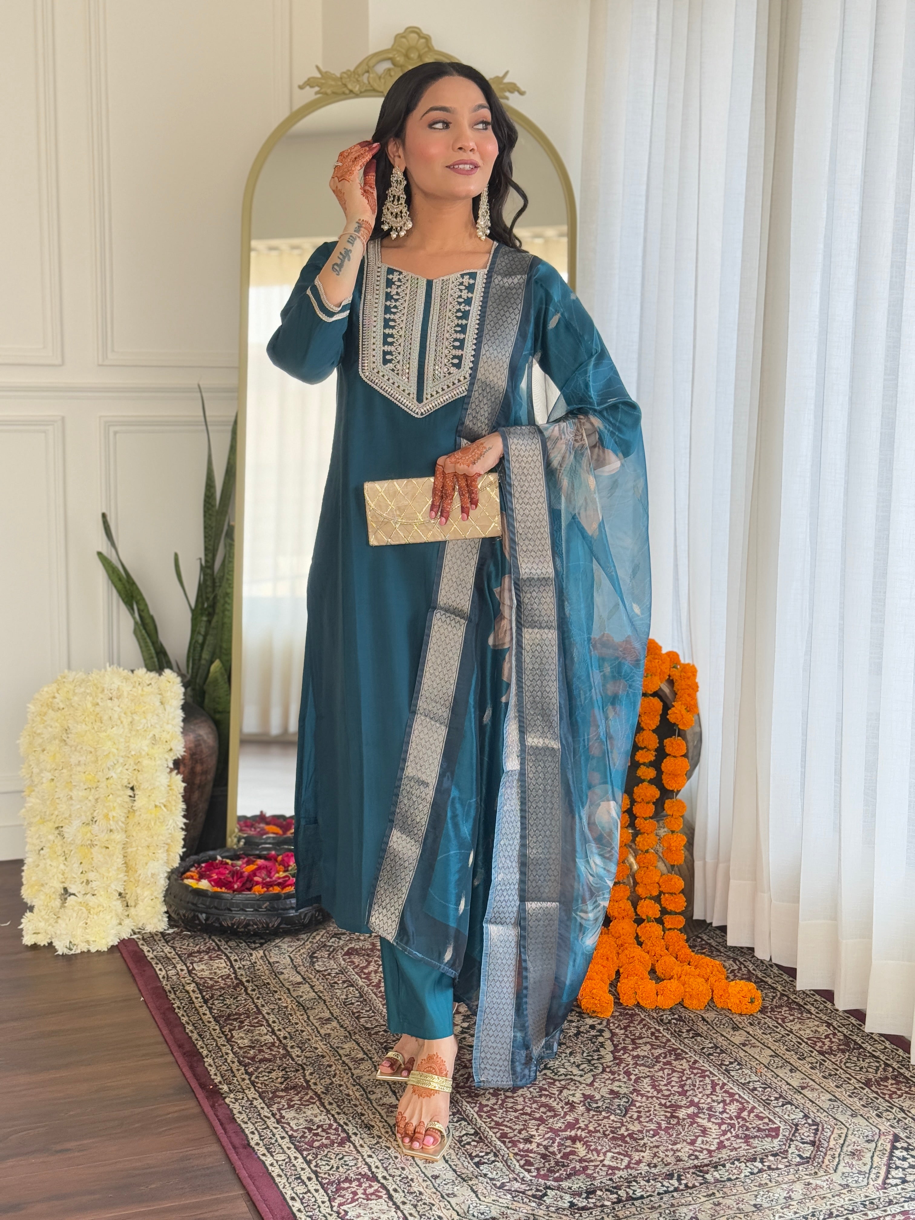 Woman gracefully adjusting her earrings while modeling the teal embroidered kurti and pant set with a flowing organza dupatta.