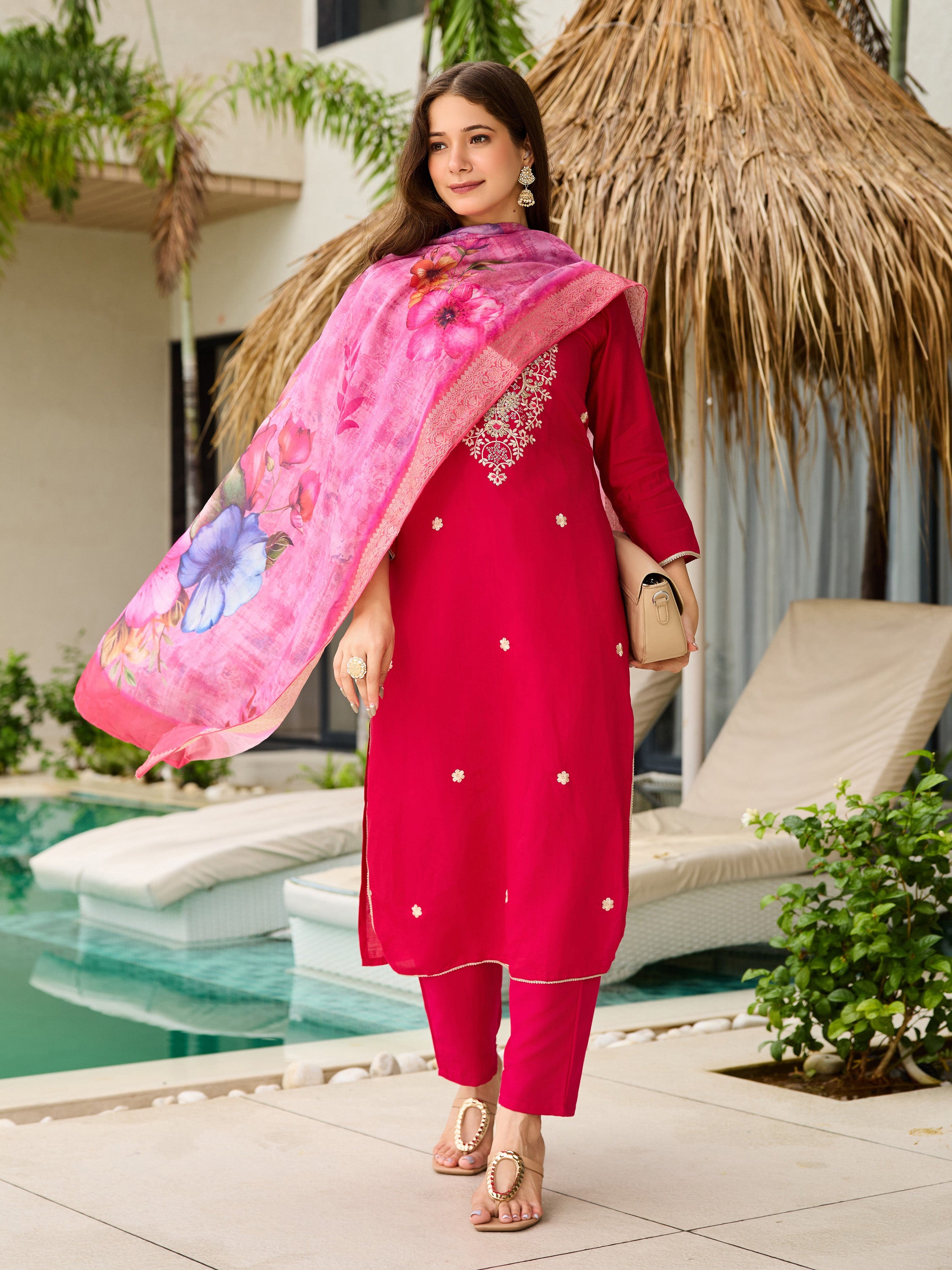 TRENDBUY model walking by the pool, showcasing the full pink embroidered kurti set with a floral dupatta and handbag.