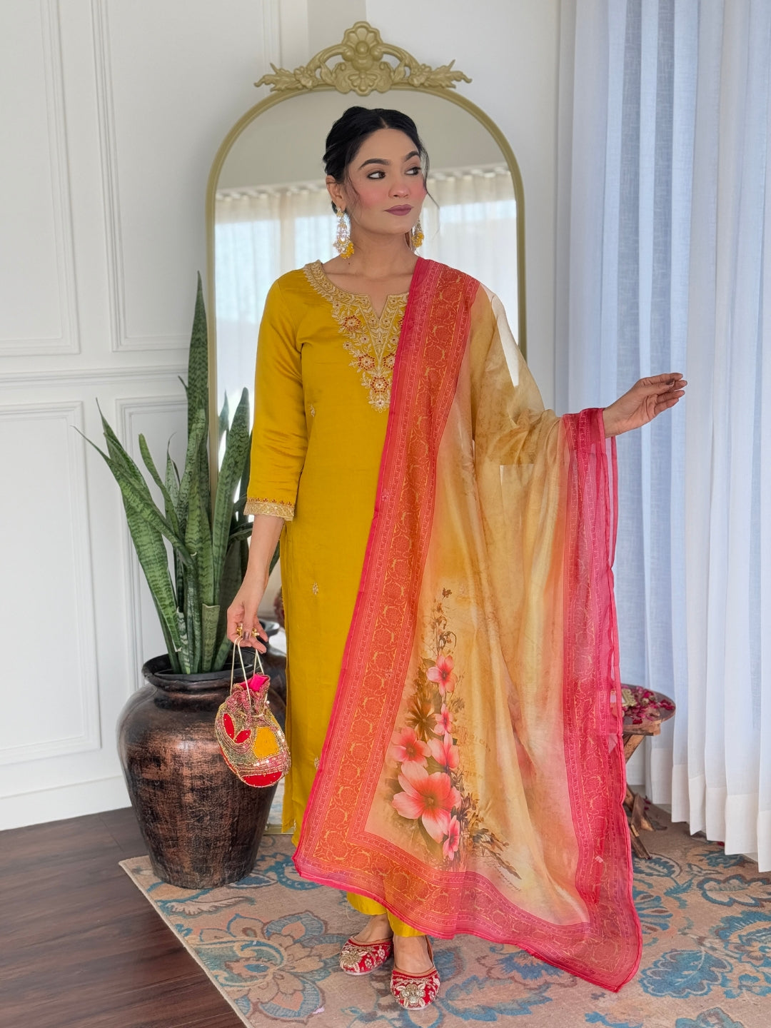 Stylish woman in the mustard kurti set with colorful floral taby dupatta, posing confidently indoors with a plant accent