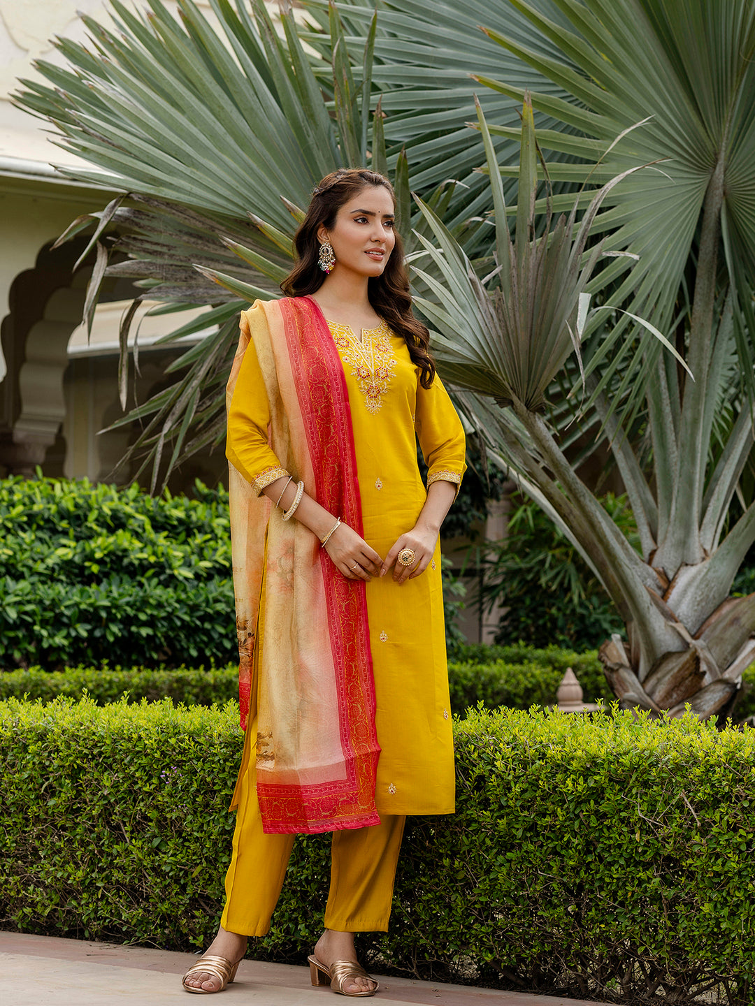 Fashionable woman in the mustard ethnic ensemble with floral dupatta, standing elegantly in an outdoor garden setting