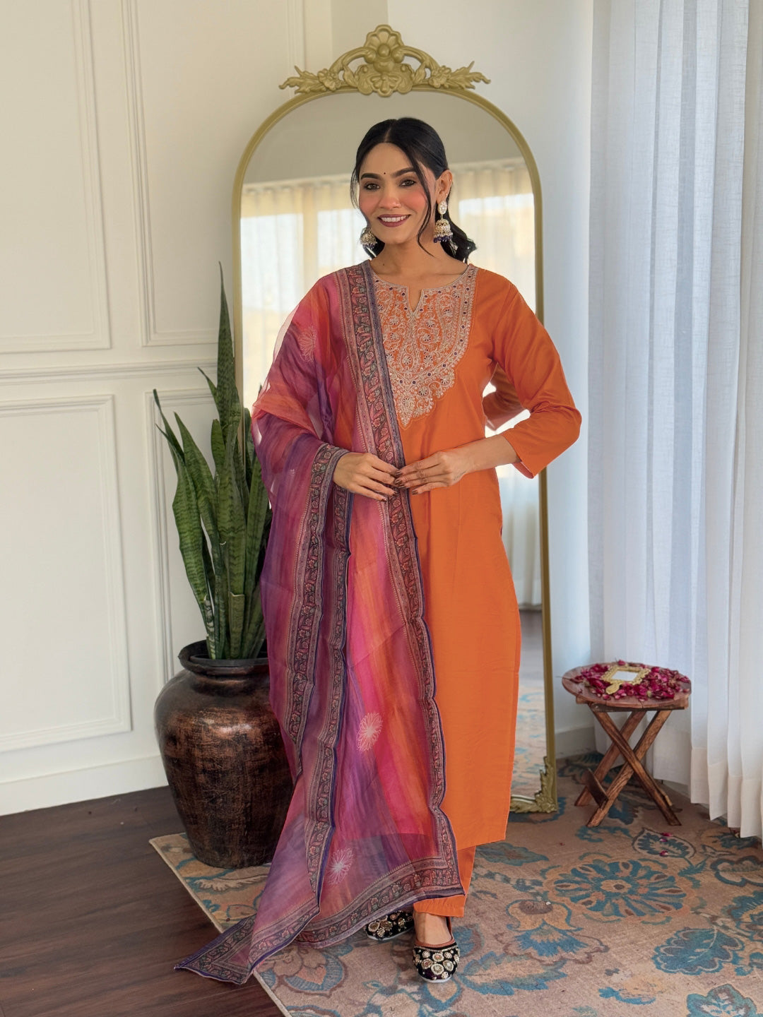 Full view of a smiling model gracefully posing in the complete orange rayon kurti, pant, and dupatta ensemble.