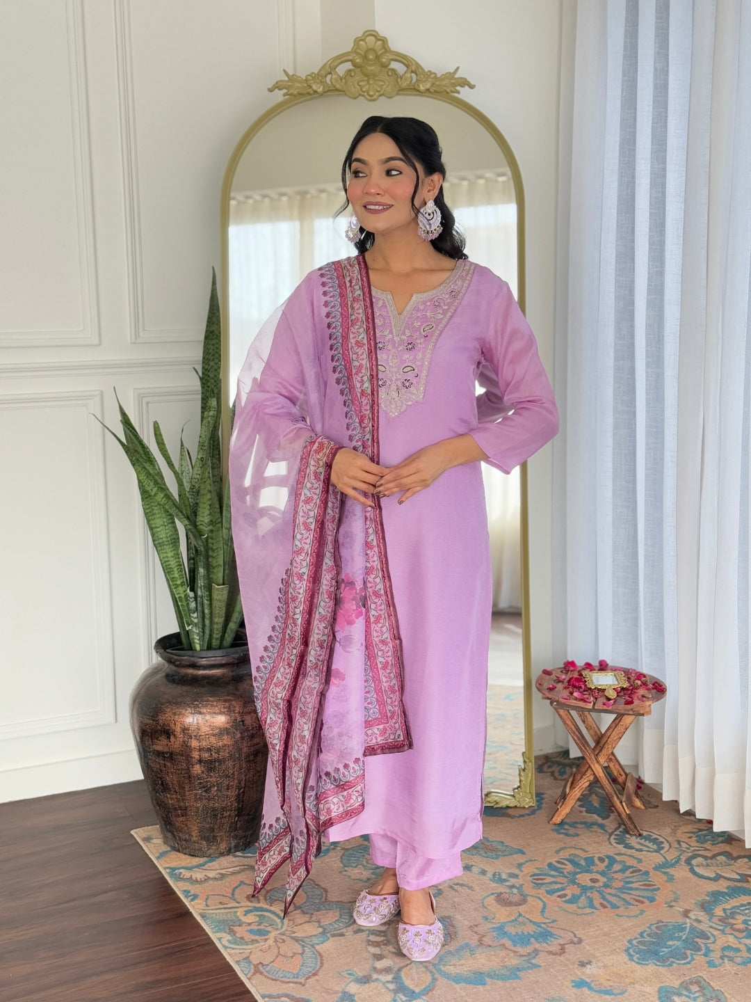 Full shot of a model wearing a lavender rayon embroidered kurta set with a printed dupatta, standing by a mirror.