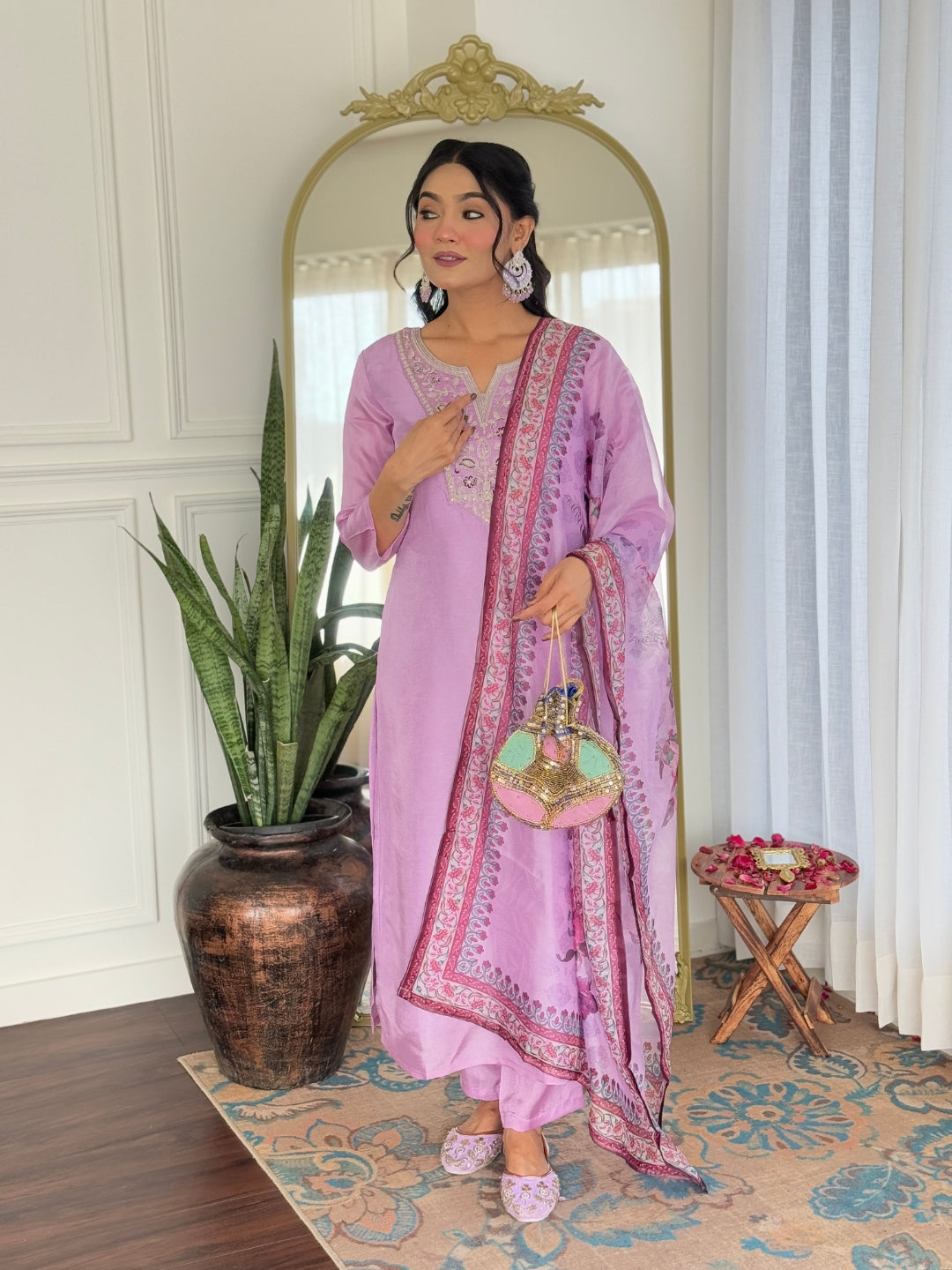 Model holding a decorative clutch, presenting the complete lavender embroidered kurti, pant, and dupatta ensemble.