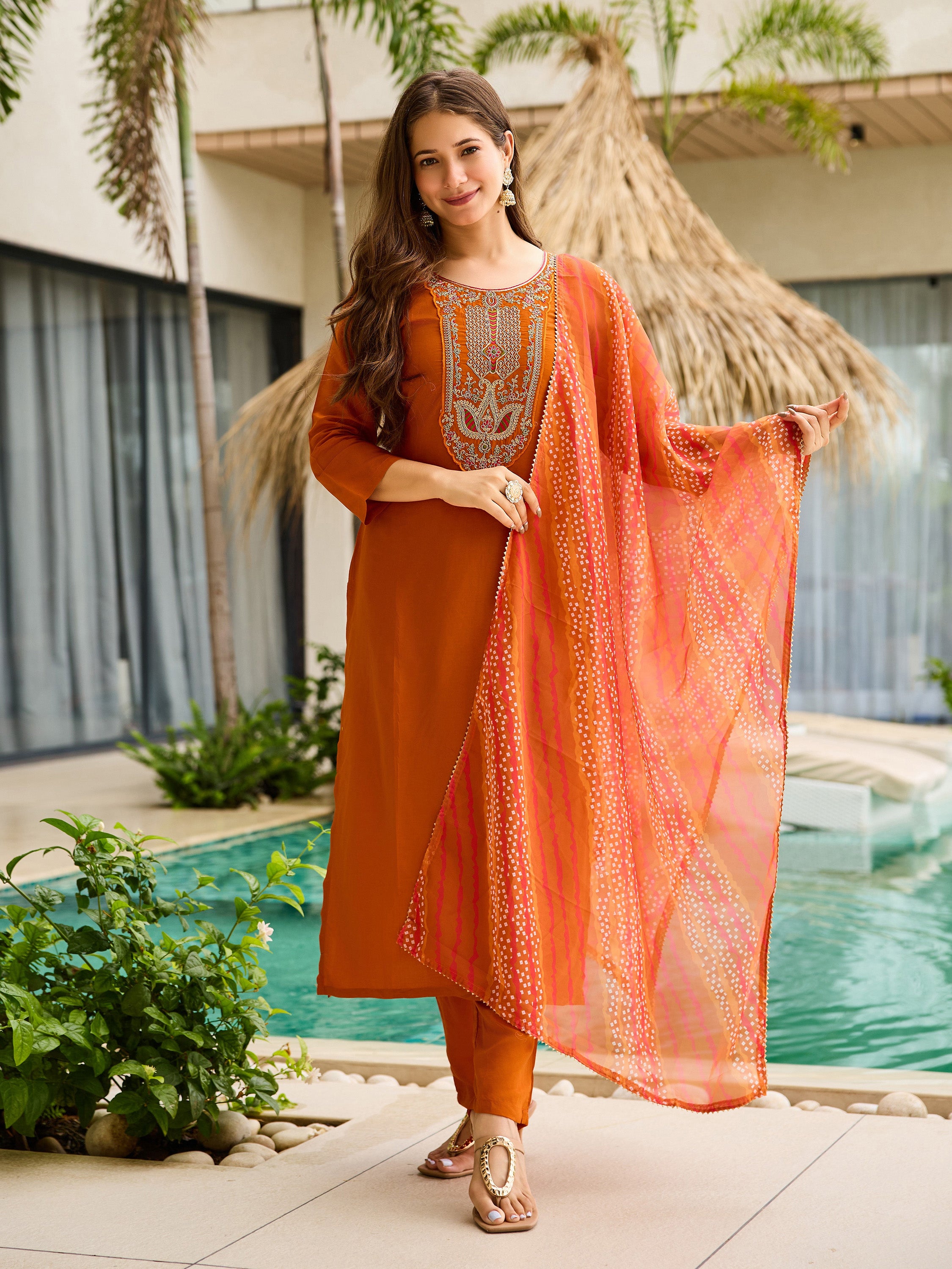 Full-length shot of model in rust orange rayon embroidered kurta set with patterned dupatta by the poolside