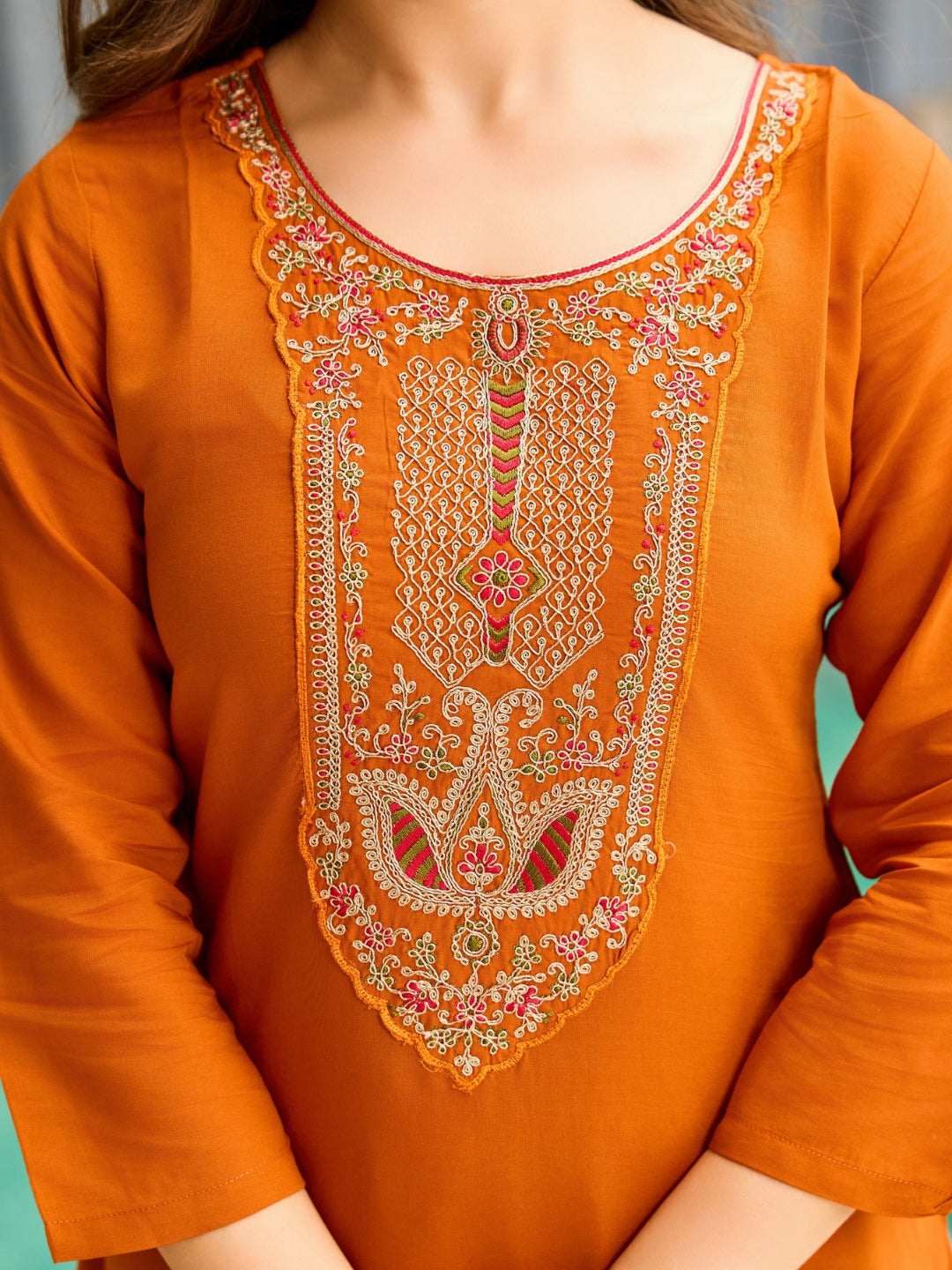 Close-up of the exquisite, multi-colored embroidery on the round neckline of the rust orange rayon kurta