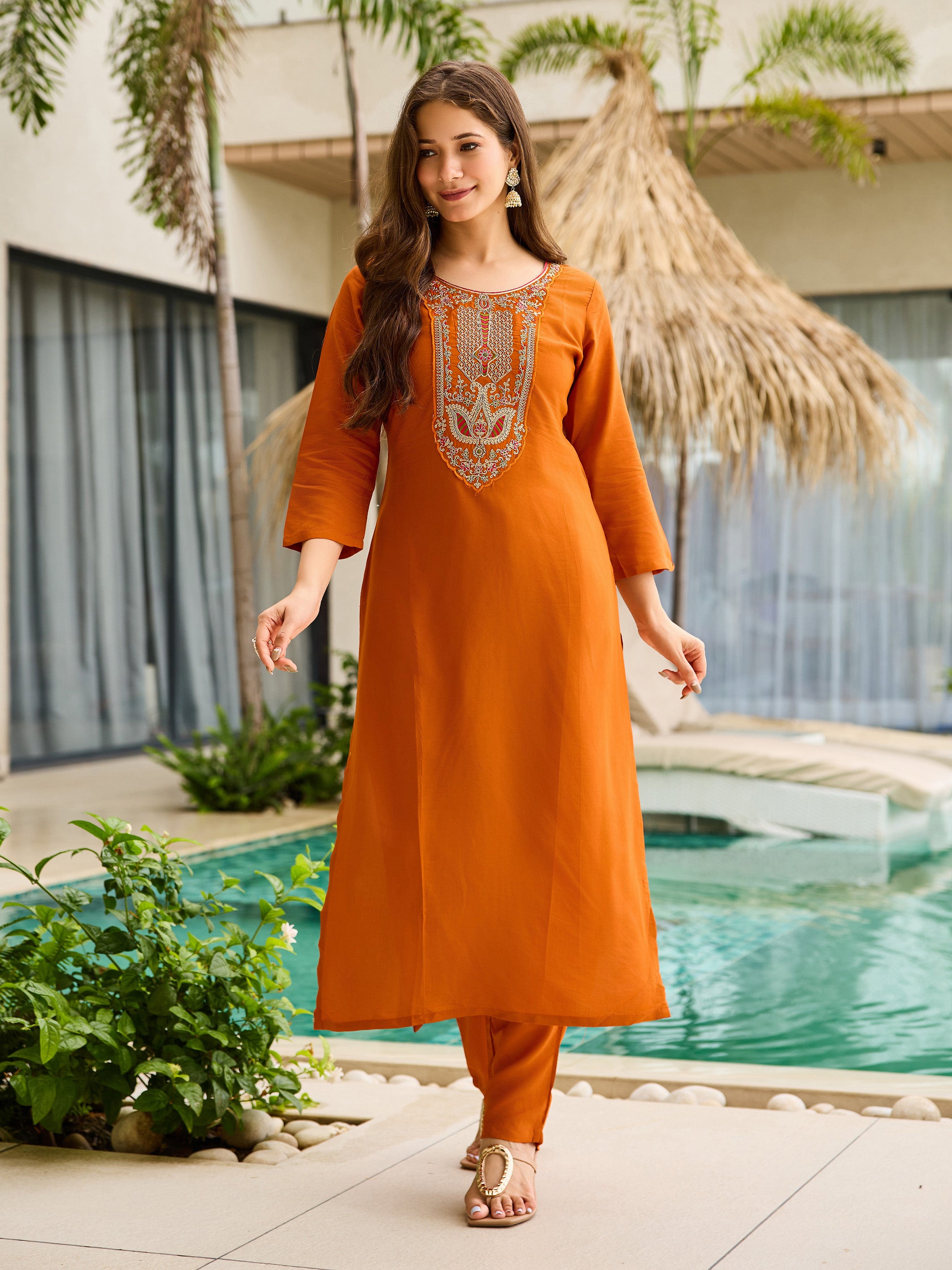 Model walking confidently in a rust orange rayon embroidered kurta pant set in a tropical outdoor setting