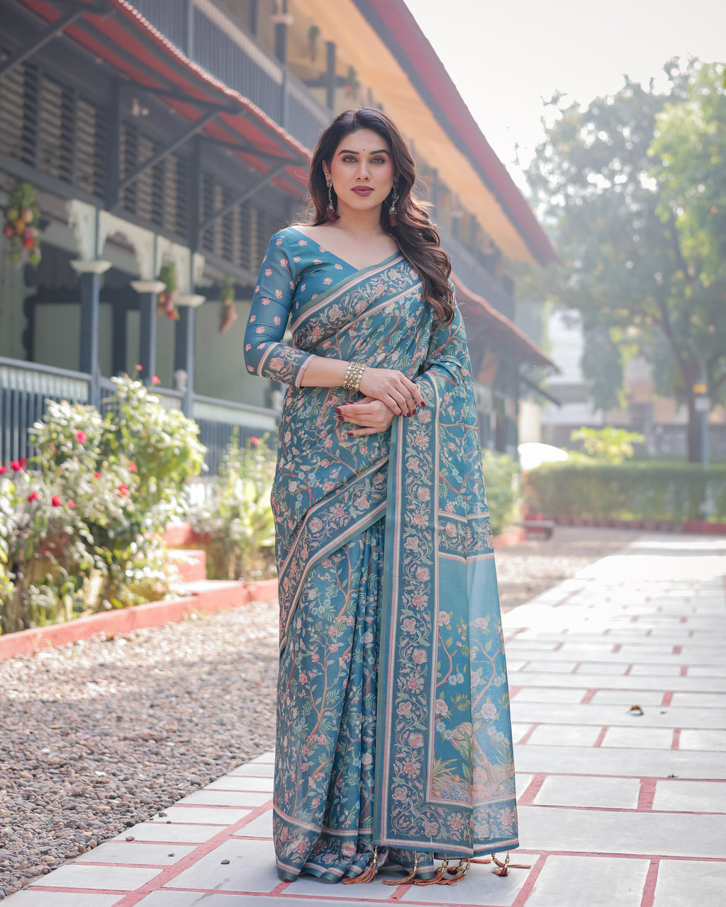 Woman posing elegantly in a teal blue handloom saree with soft floral digital print and a matching blouse, showcasing the front drape.