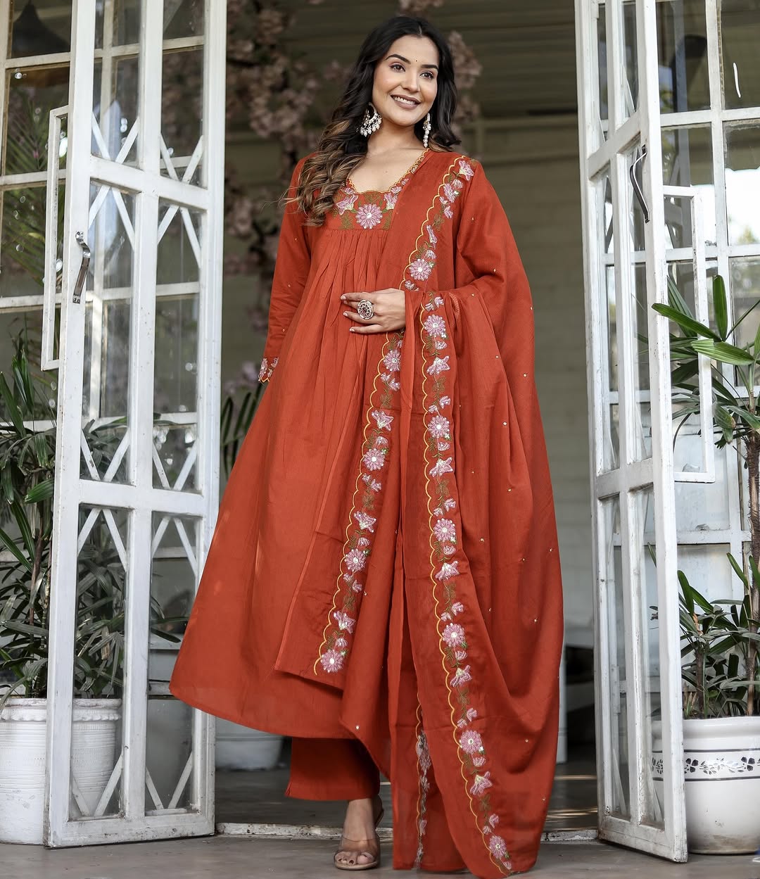 Model smiling, wearing orange rayon slub kurti set with embroidered neckline and chanderi dupatta, standing in a doorway.