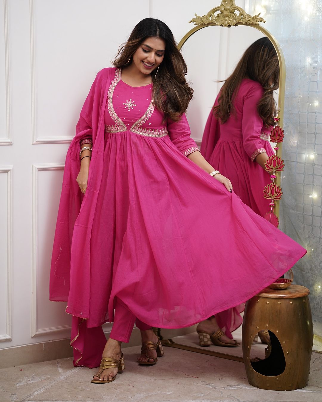 Smiling woman in a pink Muslin Cotton kurta set, gracefully lifting the hem of her kurta to show its flair and the matching pant.