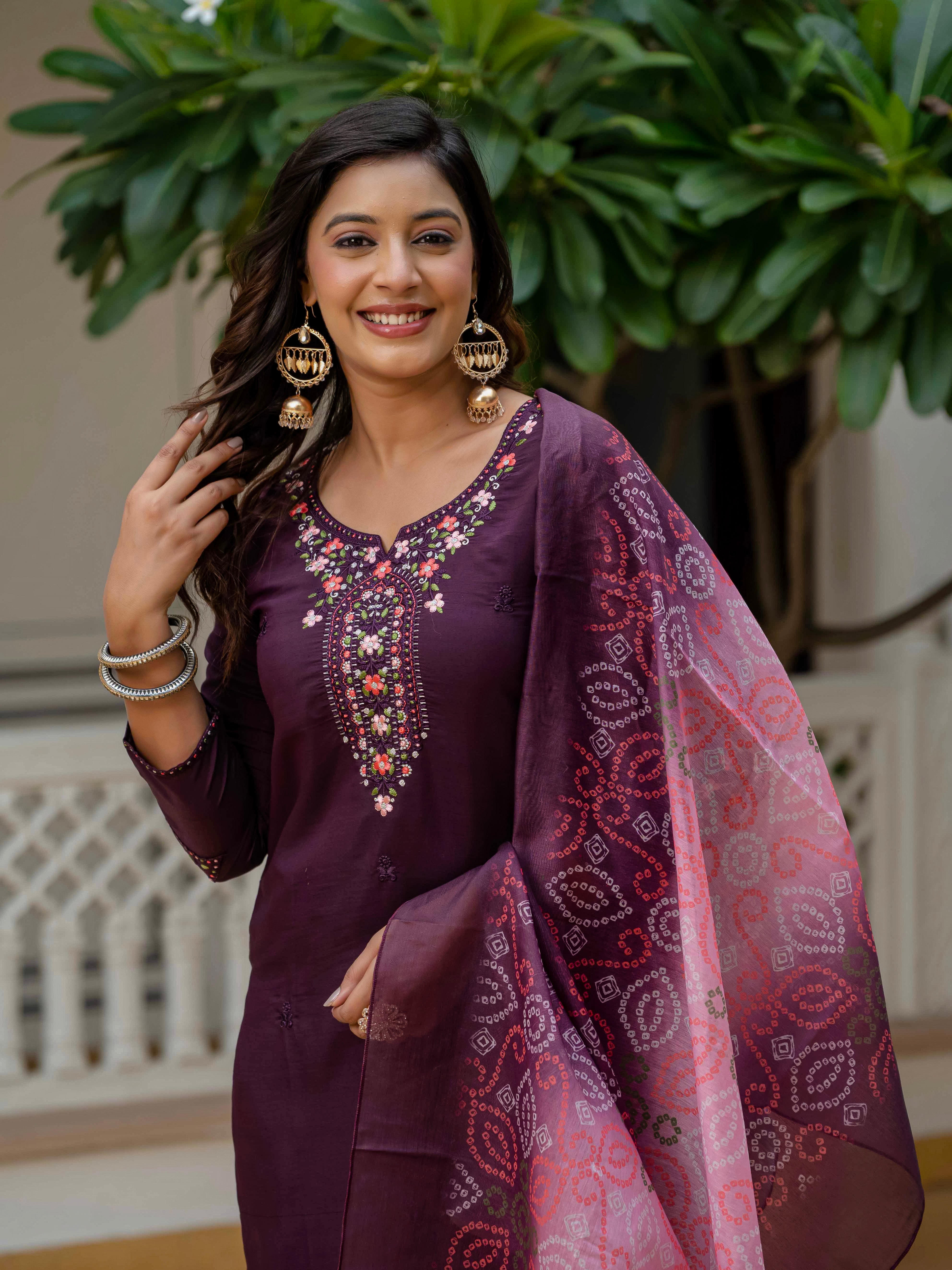 Delighted model in a close-up, highlighting the complete plum kurti set, the vibrant bandhani dupatta, and her traditional jewelry.