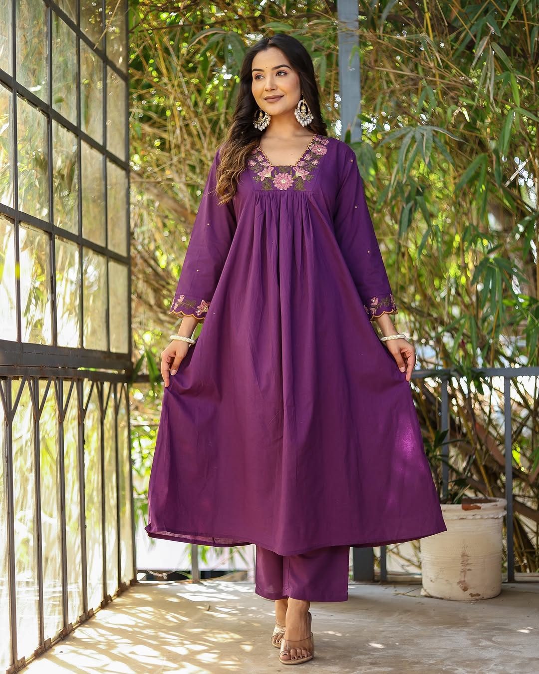 Model in full length, wearing purple rayon slub kurti set, hands holding the kurti flare, standing on a balcony.