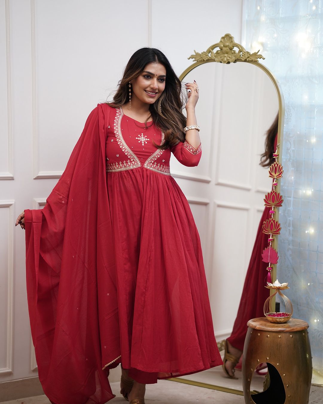 Smiling woman in a red Muslin Cotton kurta set, showcasing the flow and elegance of the outfit with one hand near her hair.