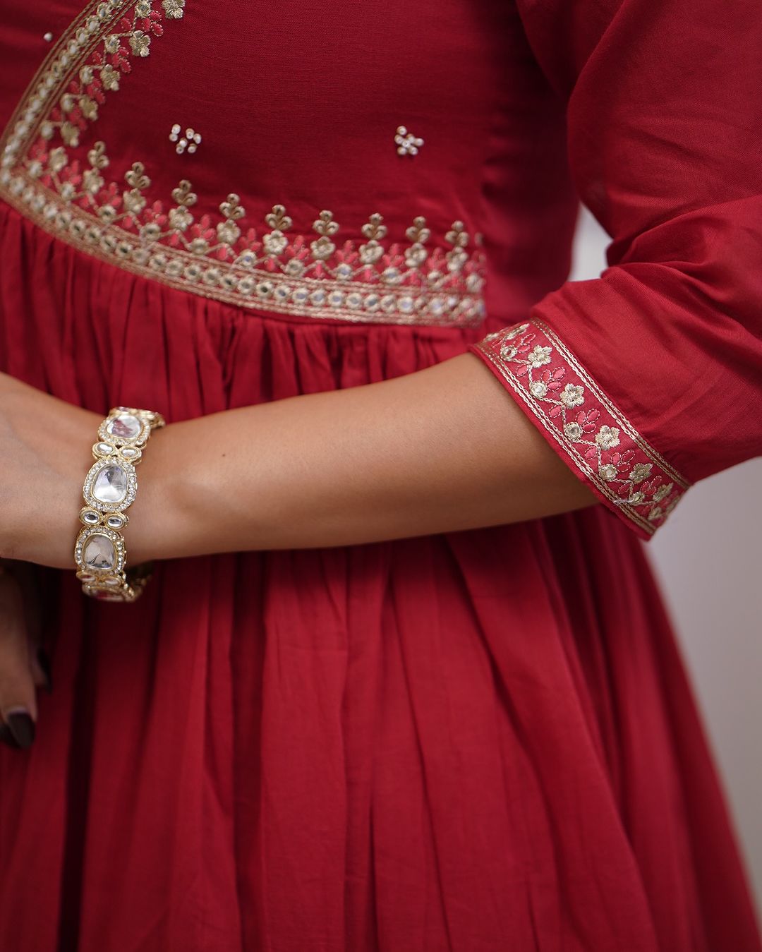 Close-up of the woman's arm in the red kurta, detailing the embroidered cuff and a sparkling bracelet.