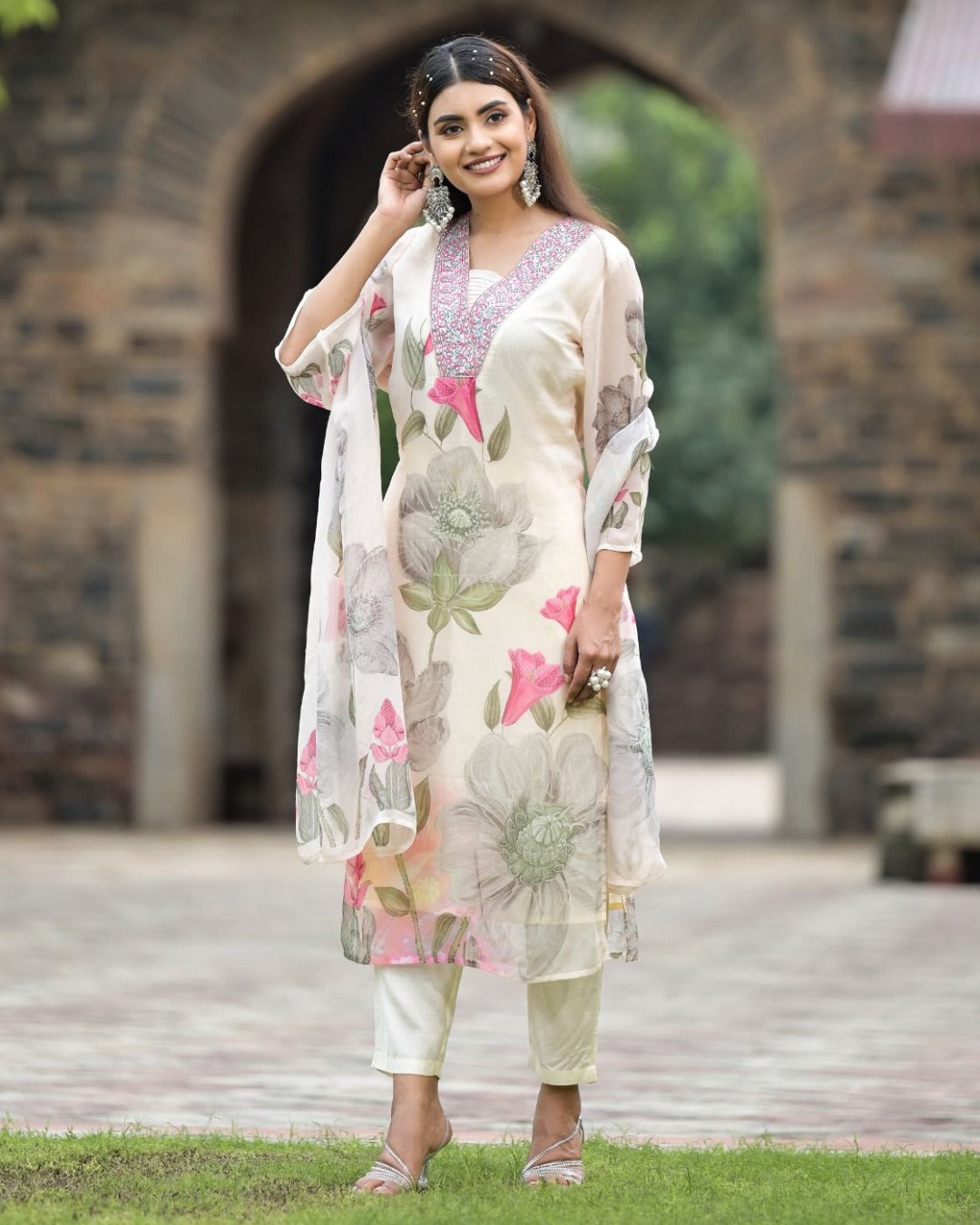Elegant woman in white Georgette Sonika kurta set, smiling and adjusting hair, featuring detailed embroidery.
