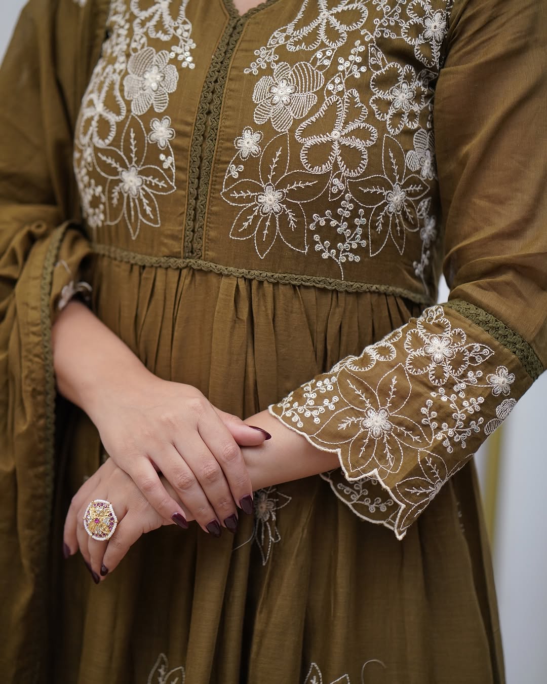 Close-up of Sapna collection olive green cotton silk gown with white floral embroidery on bodice and sleeves, showcasing delicate handwork.