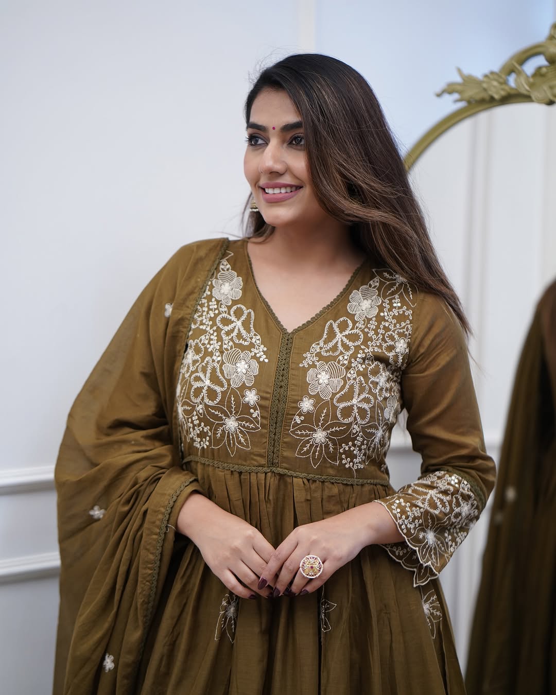 Smiling woman wearing the TRENDBUY Sapna olive green embroidered gown set, showcasing the V-neck and flowy silhouette.