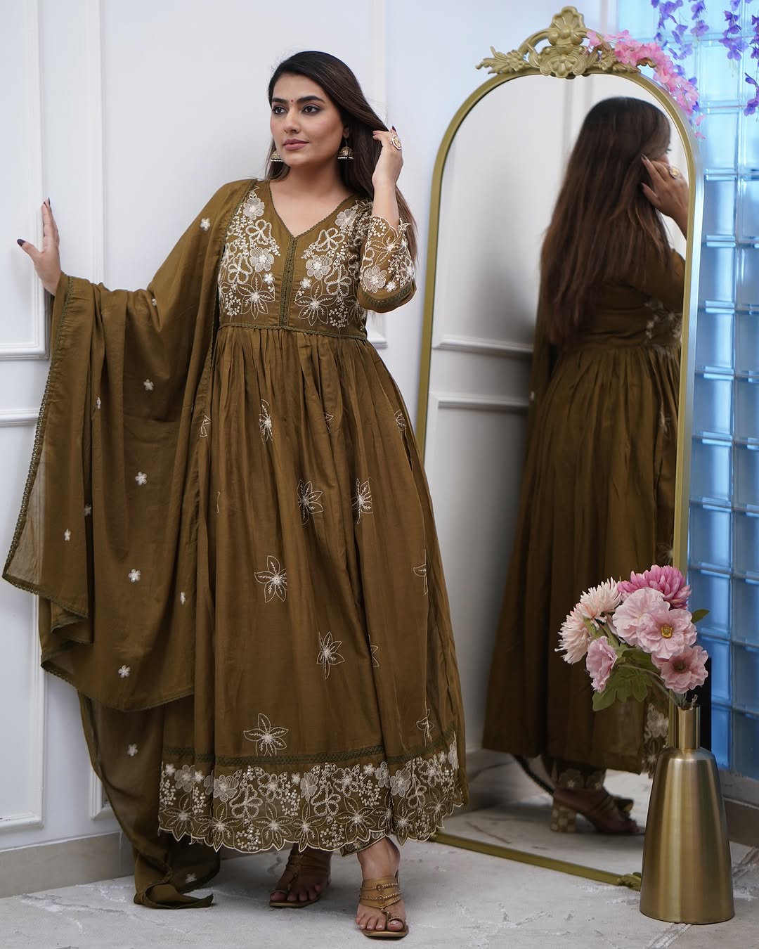 Full view of the model standing beside a mirror, wearing the TRENDBUY Sapna olive green embroidered gown with matching pant and chanderi dupatta, showcasing the overall look.