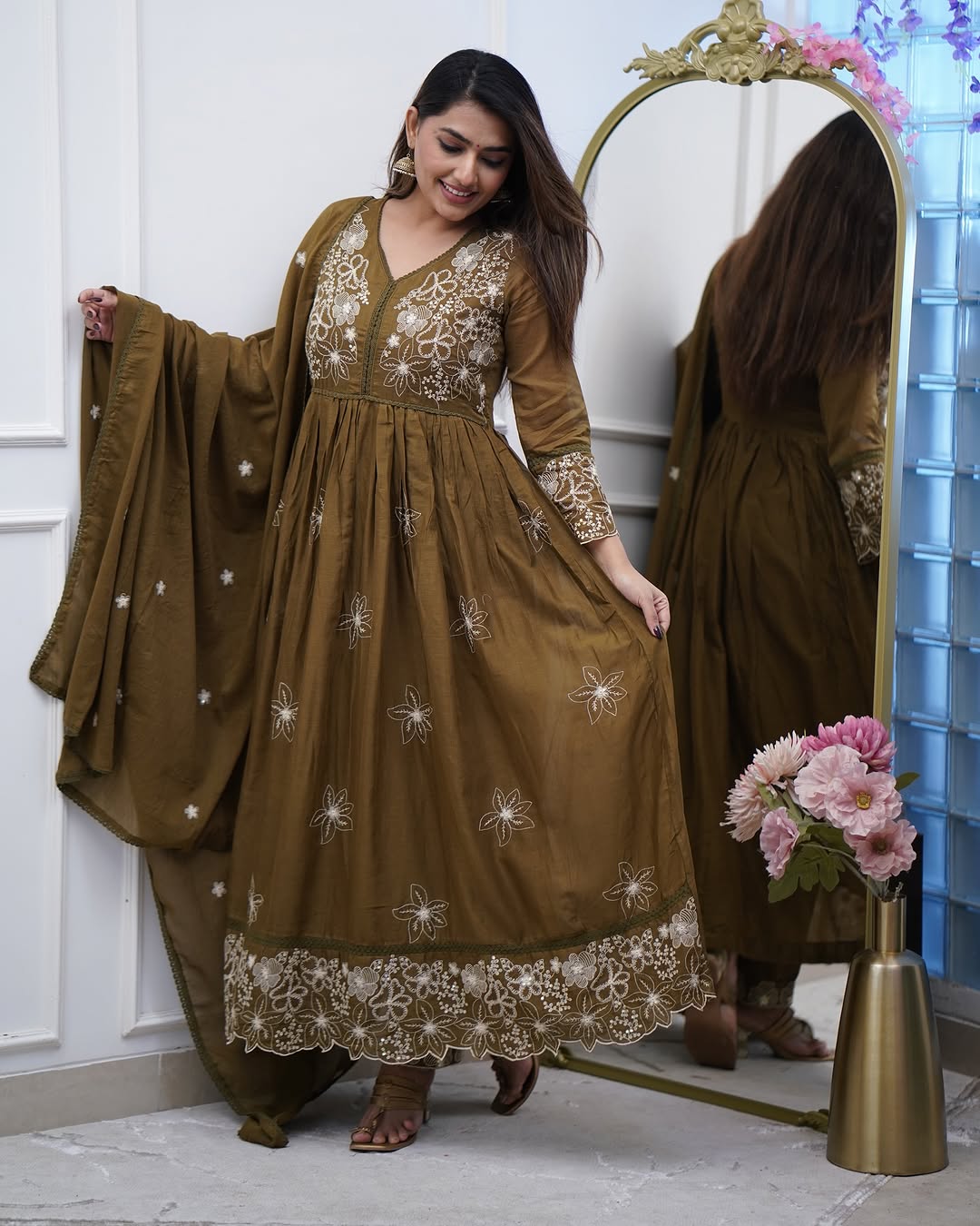 Model playfully showcasing the flair and embroidery detail on the hem of the TRENDBUY Sapna olive green cotton silk gown.
