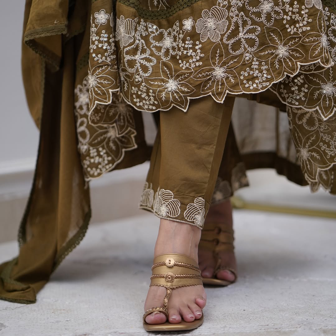Detail shot of the embroidered hem of the Sapna olive green gown and matching embroidered pant, paired with elegant sandals.