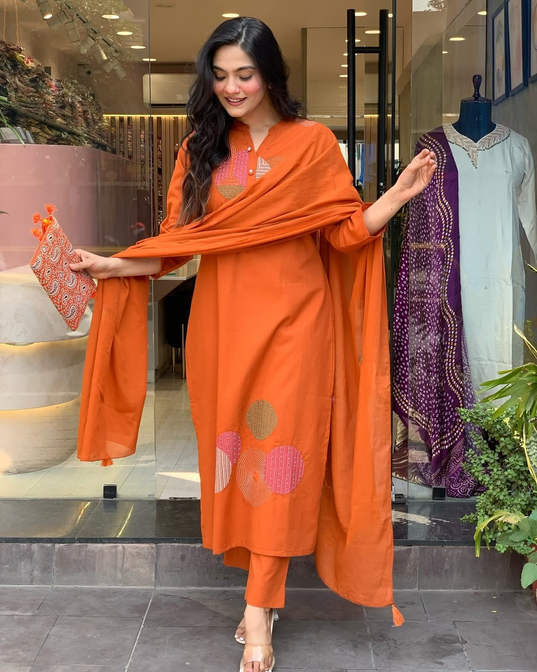Model smiling, showing the TRENDBUY ST-KASHMIRA orange embroidered kurti set with a matching clutch