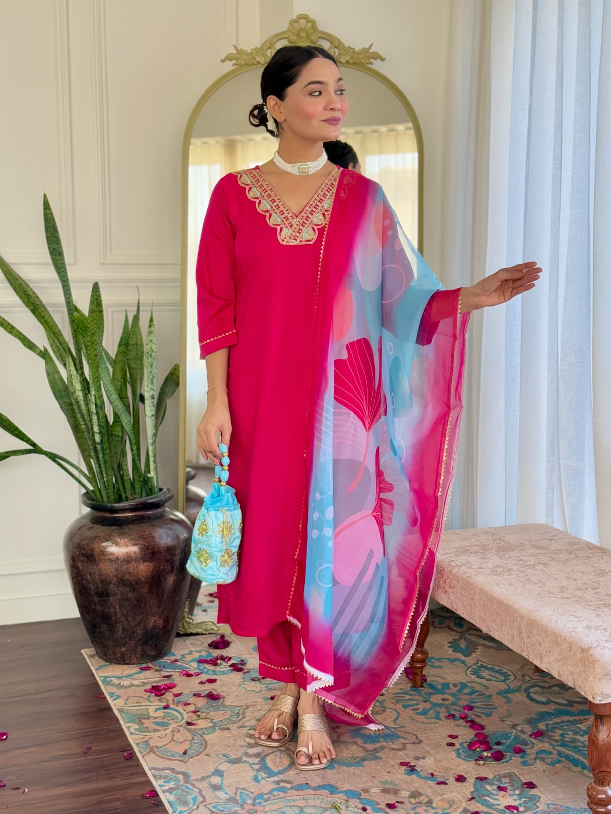 Woman posing elegantly in a hot pink rayon kurti set with embroidered V-neck and a vibrant printed Teby silk dupatta, holding a blue potli bag.