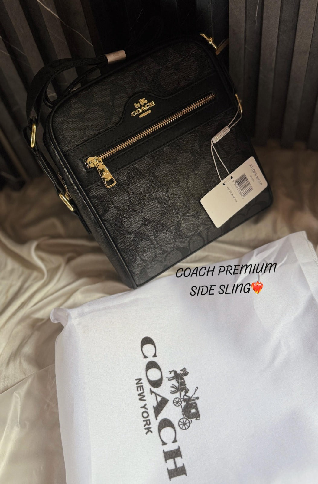 A Coach signature crossbody sling bag in black with a leather-textured exterior, metallic COACH logo, and a white dust cover with the brand name printed on it.