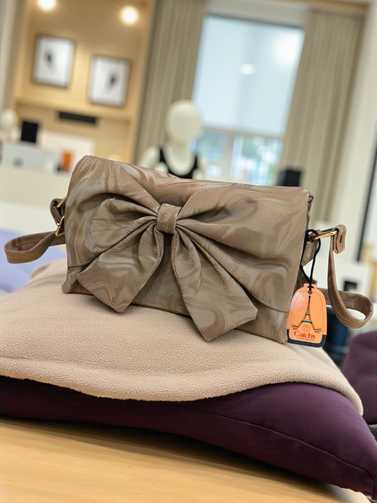 Beige handbag with a large bow on a cushion in an indoor setting