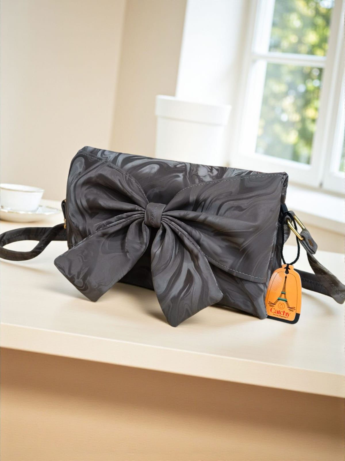 Black clutch bag with a large bow on a white surface near a window