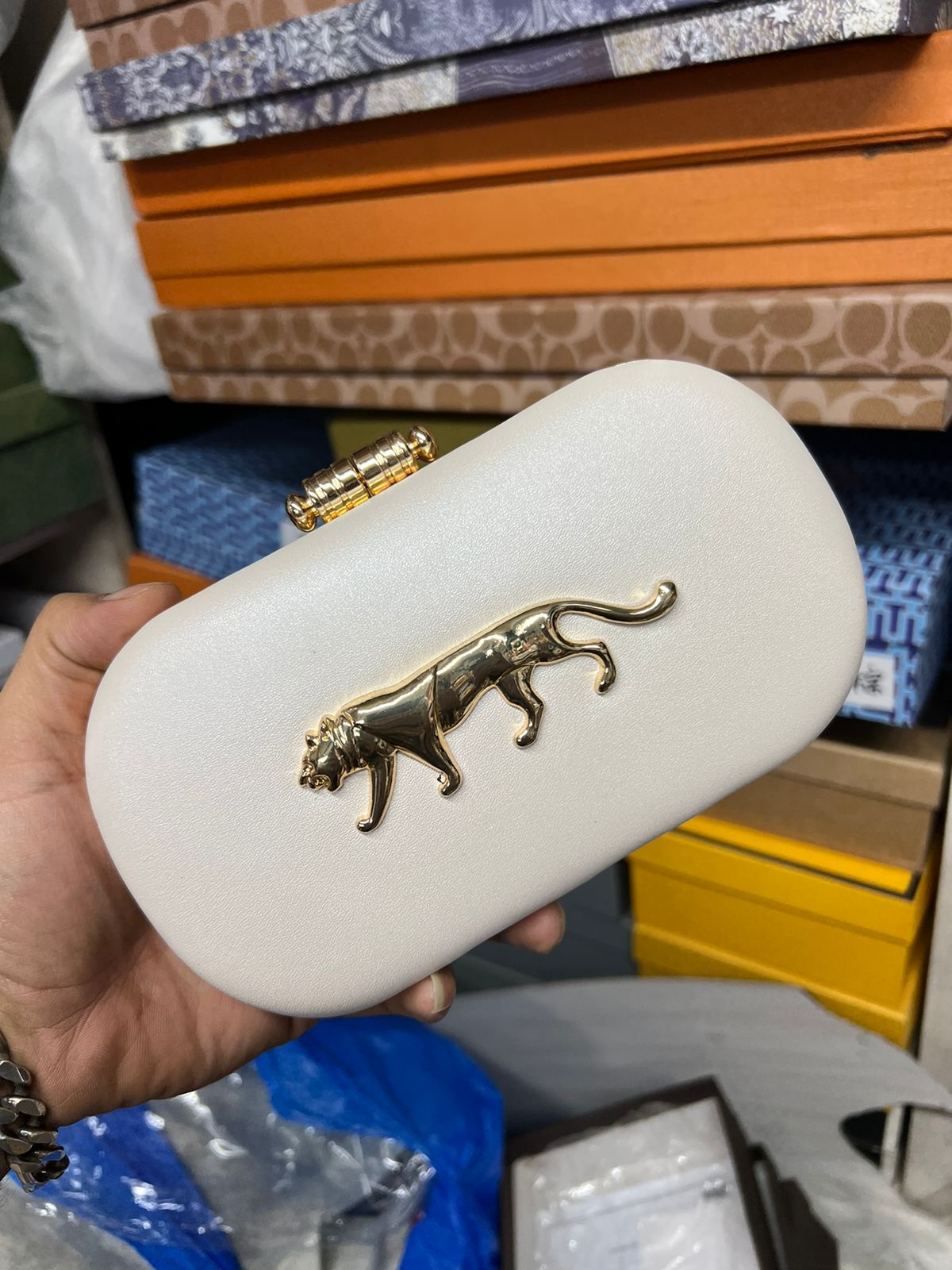 White clutch with gold panther design held by a hand against a blurred background