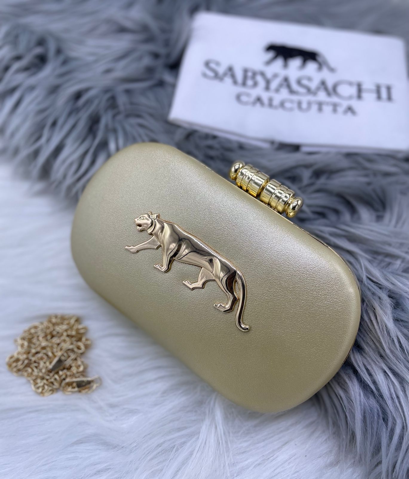 A luxurious gold evening clutch featuring the iconic Sabyasachi tiger emblem