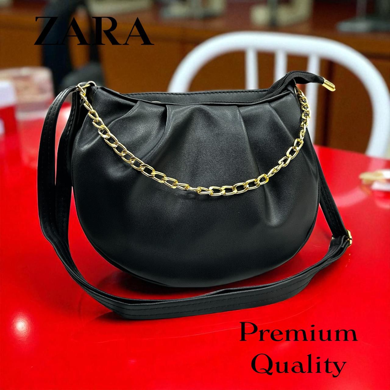 Black handbag with gold chain strap on a red surface, Zara brand visible