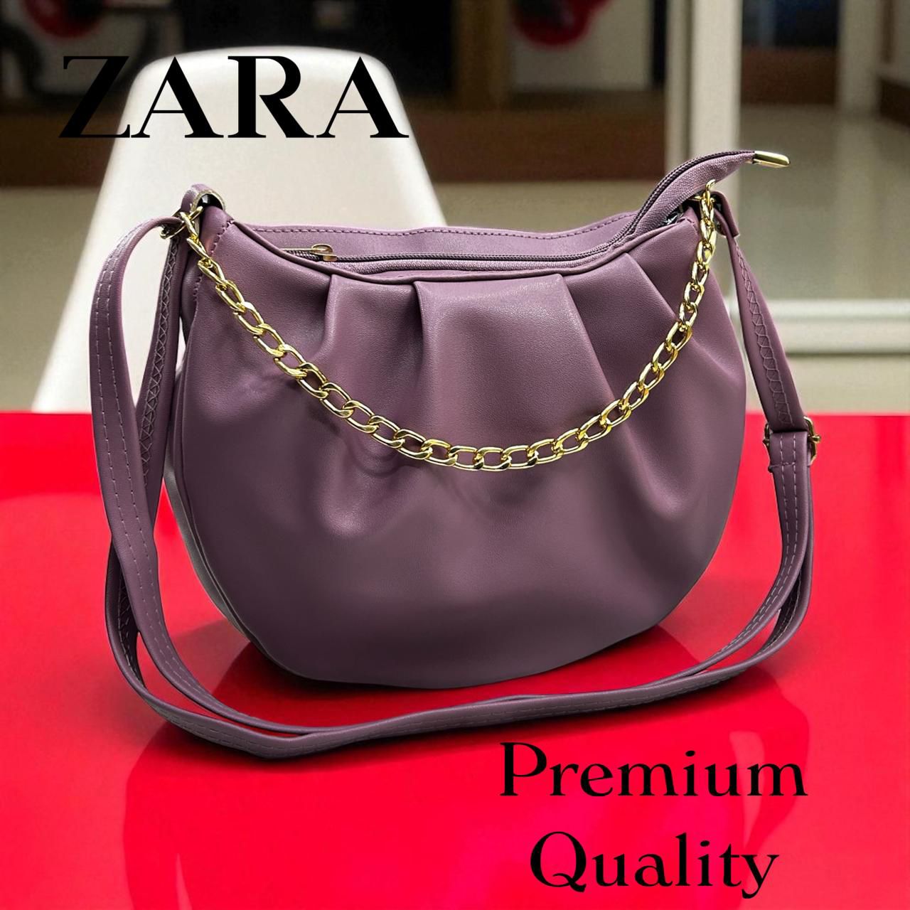 Purple handbag with gold chain on a red surface, featuring Zara branding.