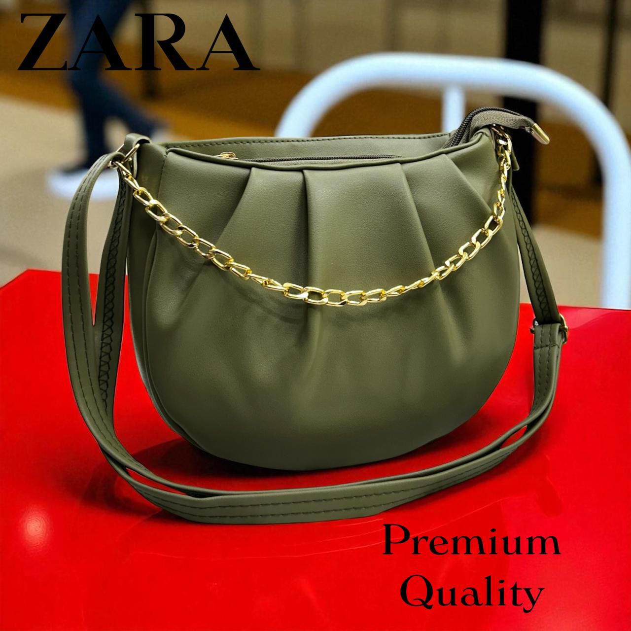 Green handbag with gold chain on a red surface, featuring Zara branding.
