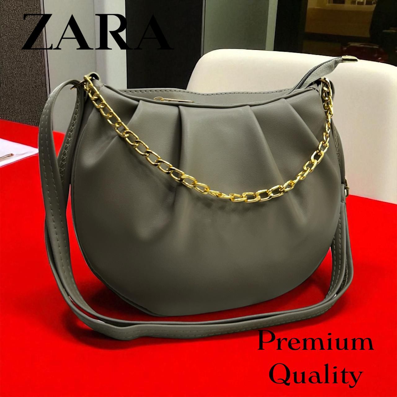 Gray handbag with gold chain on a red surface, featuring Zara branding.