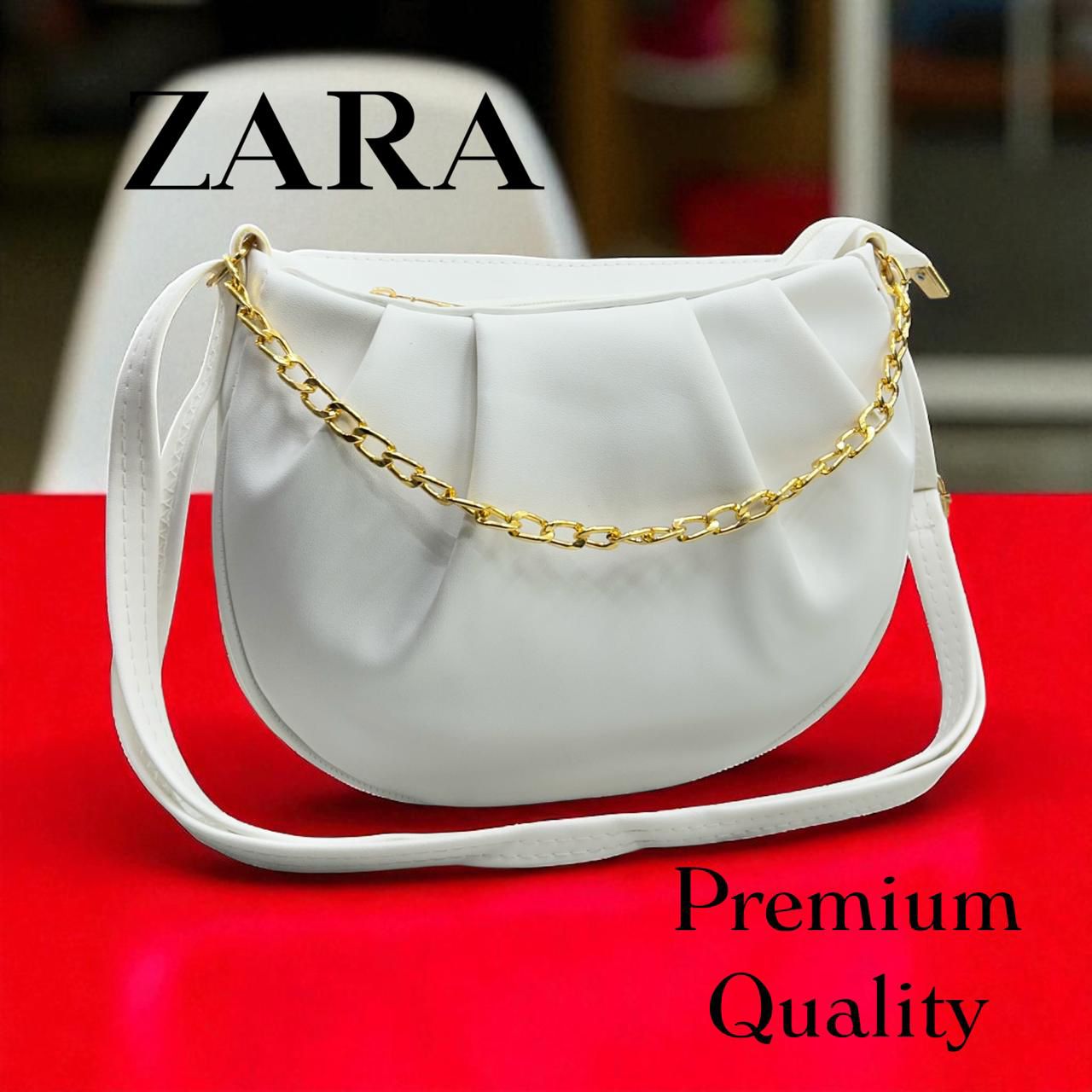 White handbag with gold chain strap on a red surface, featuring Zara branding.
