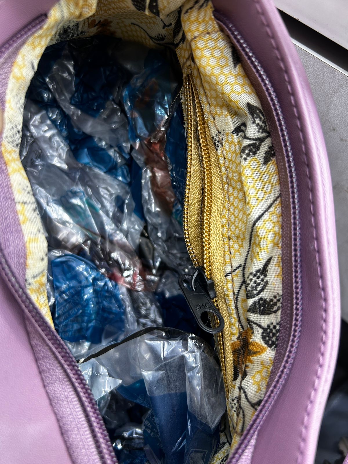 Open purple bag with floral pattern showing blue and clear plastic items inside.
