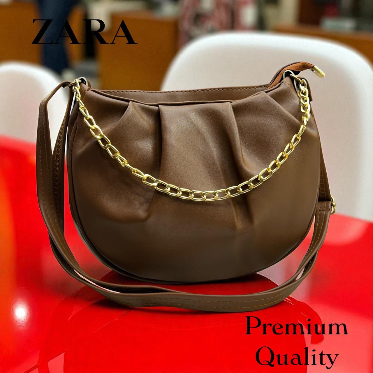 Brown handbag with gold chain on a red surface, featuring Zara branding.