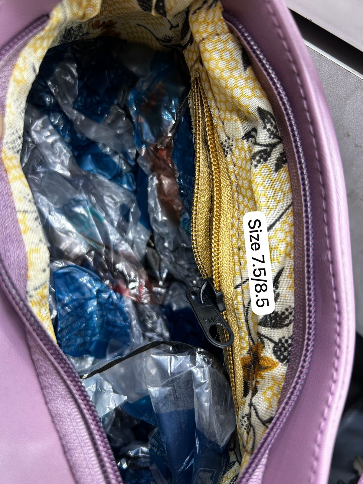 Purple bag with floral pattern and zipper, containing blue items and a label with size information.