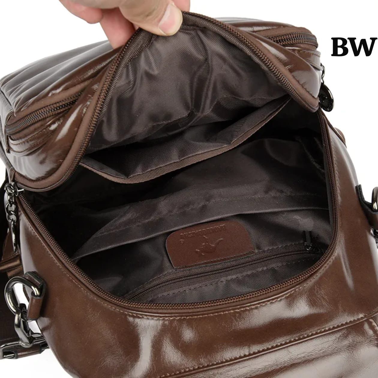 Brown leather bag with open top showing interior, held by a hand.