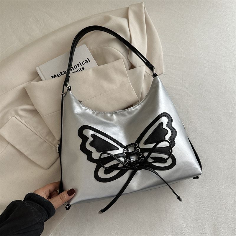 Silver handbag with a black butterfly design held by a hand on a light background