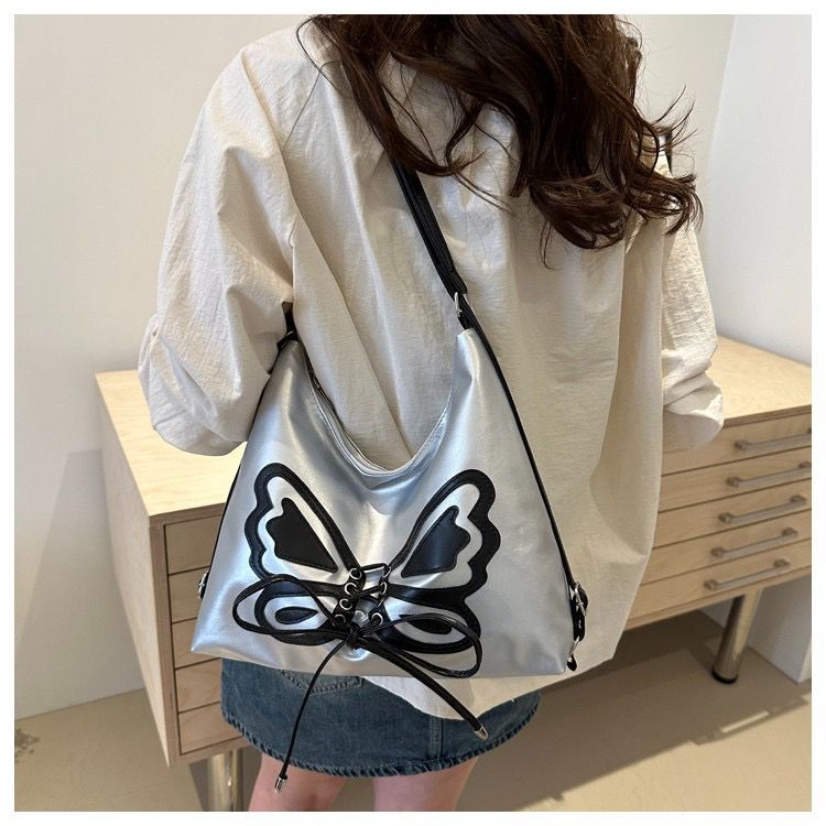 Person wearing a silver bag with a butterfly design in a minimal indoor setting