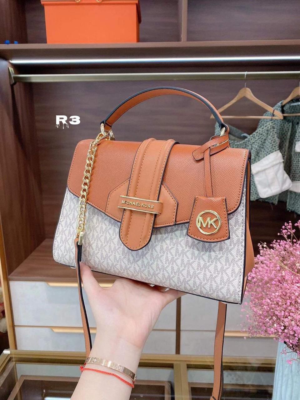 Michael Kors shoulder bag with a stylish brown and white monogram pattern, featuring a gold chain detail and a chic front flap closure.